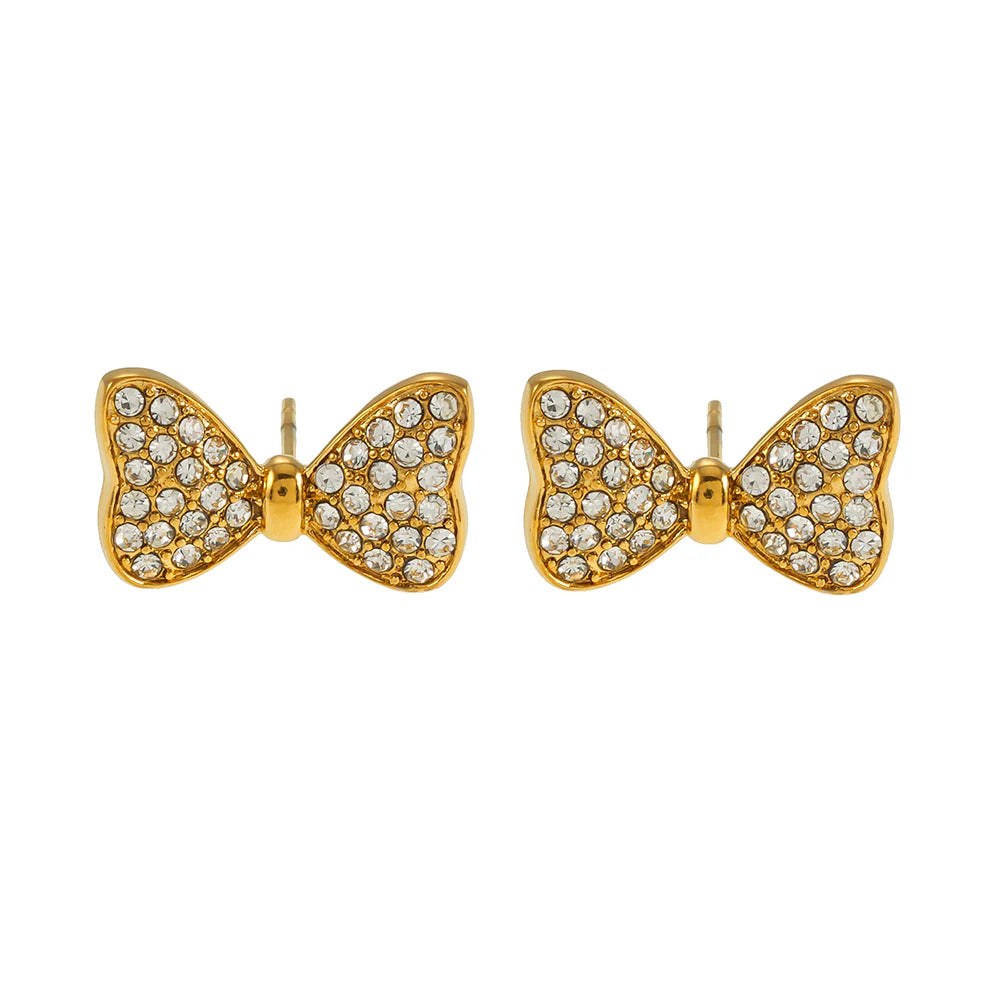 Hackney Nine Bowen gold stud earrings feature an elegant bow design adorned with sparkling pave-set cubic zirconia stones. Lightweight and hypoallergenic, they're comfortable for sensitive ears and secured with a reliable push-back closure. Perfect for both formal occasions and everyday wear, these versatile earrings add a touch of glamour to any look.