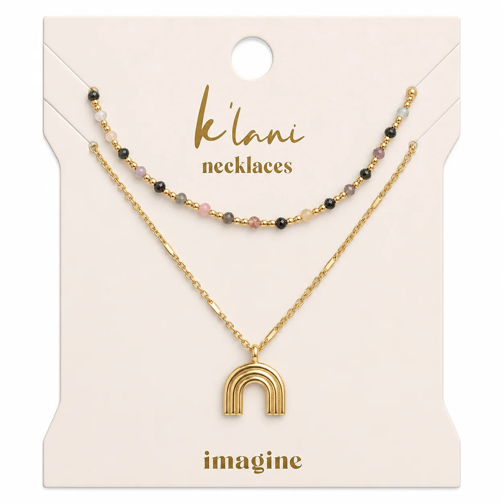 The K'lani Imagine necklace set celebrates creativity and hope through vibrant design. One necklace features colorful glass and gold beads, while the second showcases a gold rainbow charm on a detailed chain. Layer them together for inspired, limitless style.
