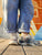 Person wearing blue jeans and Merrell J038916  patterned sneakers on a wooden floor with a colorful wall in the background